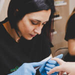 Onicotecnica che esegue una manicure professionale limando le unghie di una cliente, indossando guanti e lavorando con cura.