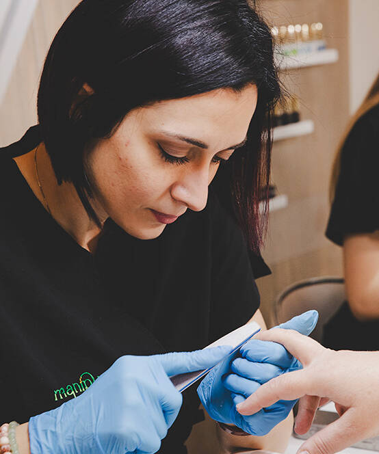 Onicotecnica che esegue una manicure professionale limando le unghie di una cliente, indossando guanti e lavorando con cura.