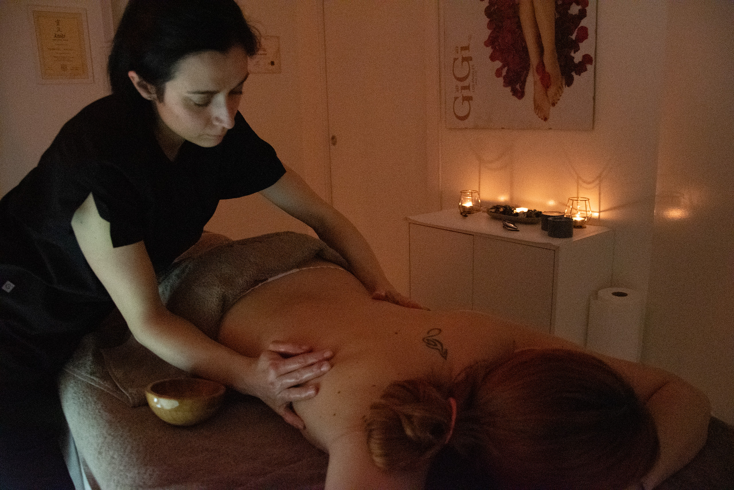 Estetista che esegue un massaggio rilassante alla schiena in una cabina con luci soffuse e candele accese.