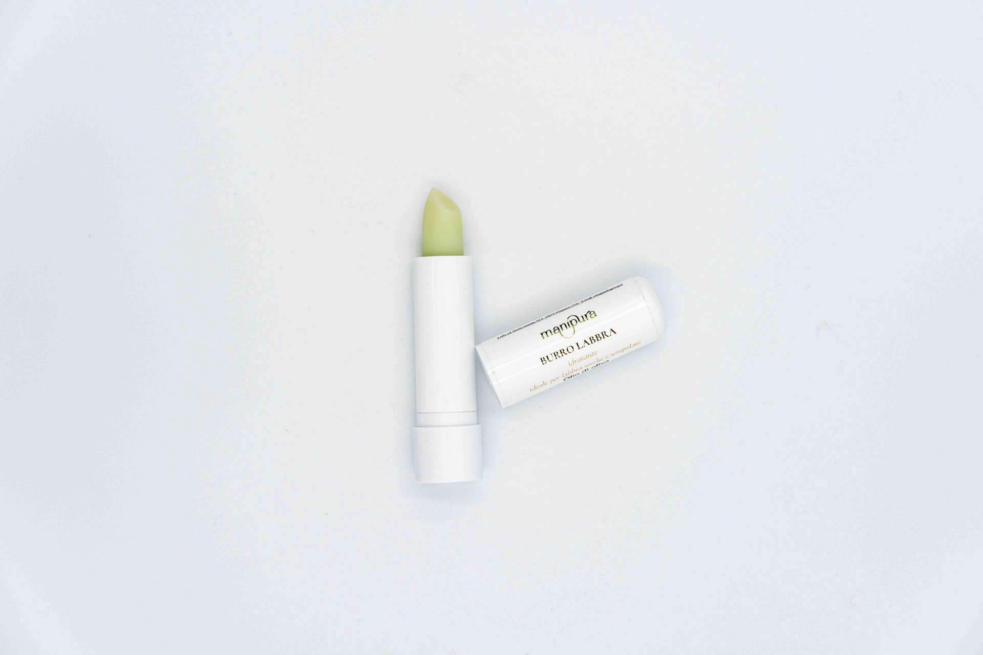 Stick burro labbra Manipura aperto con tappo appoggiato accanto su sfondo bianco.