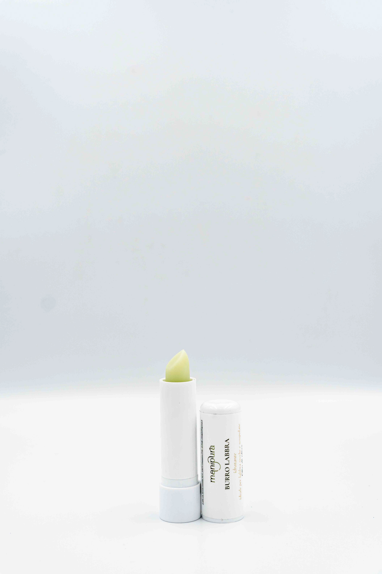 Stick burro labbra Manipura aperto con tappo appoggiato accanto su sfondo bianco.