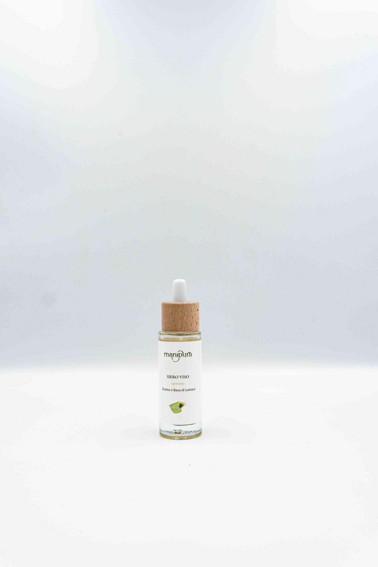 Flacone di siero viso rigenerante Manipura con enzima e bava di lumaca, dotato di contagocce con tappo in legno, su sfondo bianco.