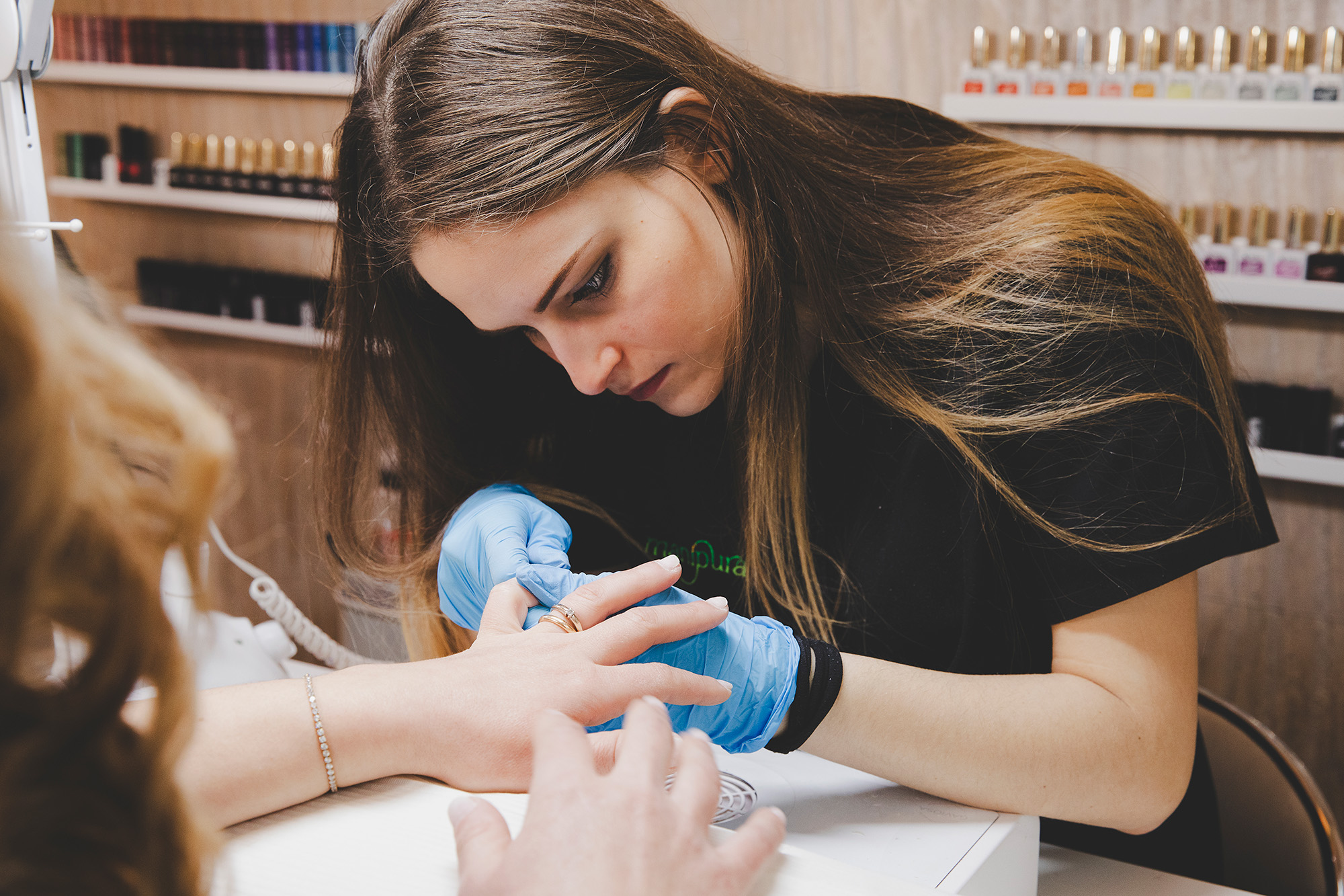 Onicotecnica che cura le unghie di una cliente con precisione, indossando guanti blu durante la manicure.