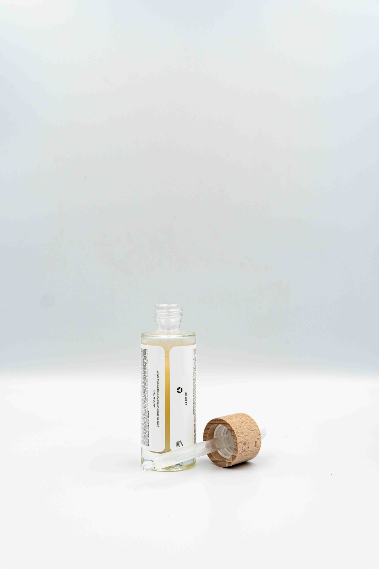 Flacone aperto del siero viso alla bava di lumaca Manipura visto dal retro, con contagocce appoggiato e tappo in legno su sfondo bianco.