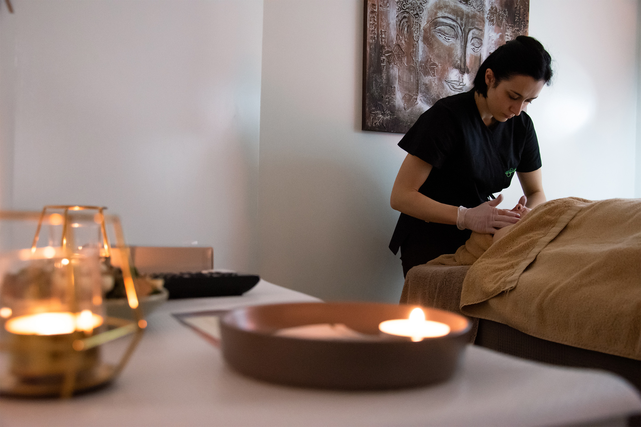 Estetista che esegue un trattamento viso rilassante in cabina con atmosfera spa e candele accese.