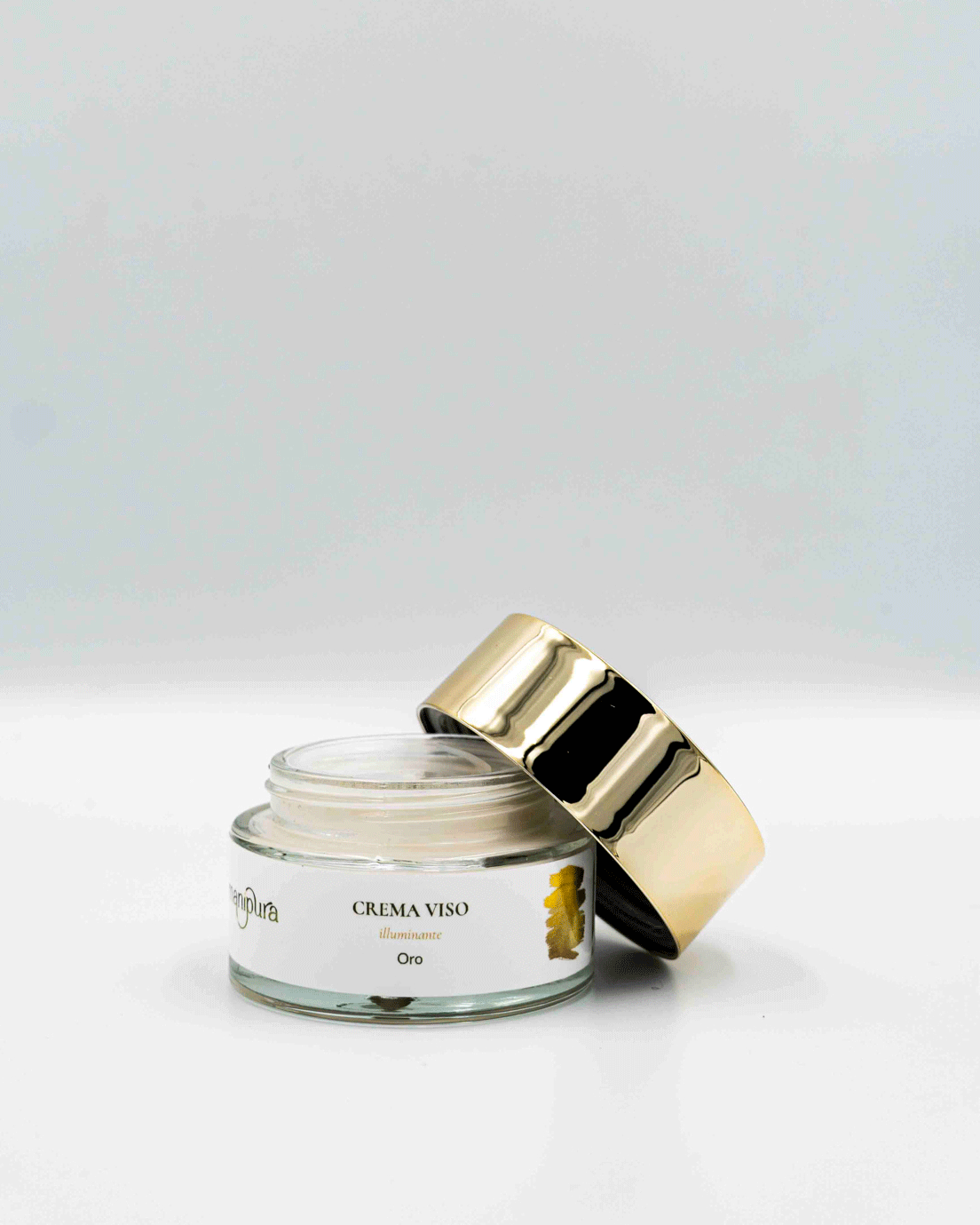 Vaso aperto di crema viso illuminante Oro di Manipura con coperchio dorato appoggiato lateralmente, fotografato su sfondo bianco.