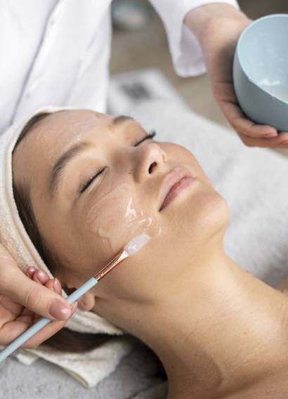 Estetista applica una maschera viso con pennello durante un trattamento skincare rilassante.