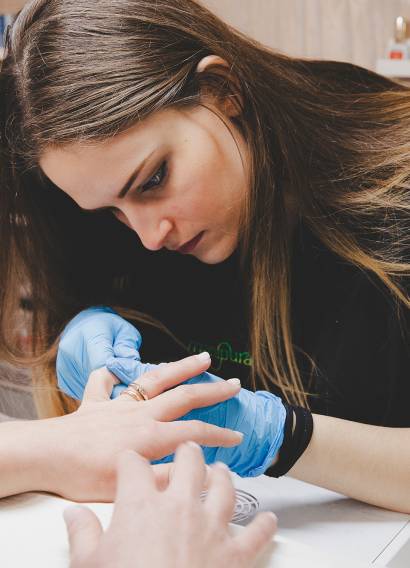 Onicotecnica che cura le unghie di una cliente con precisione, indossando guanti blu durante la manicure.
